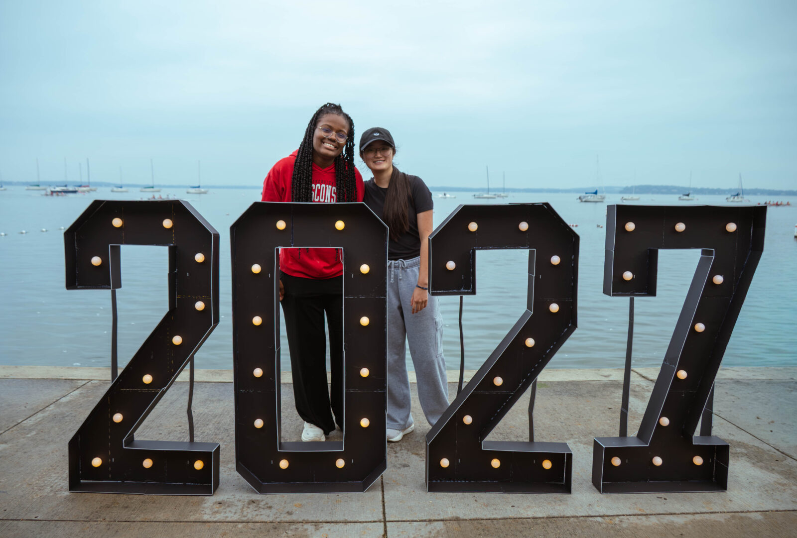 Two seniors pose next to the 2029 sign in front of Lake Mendota